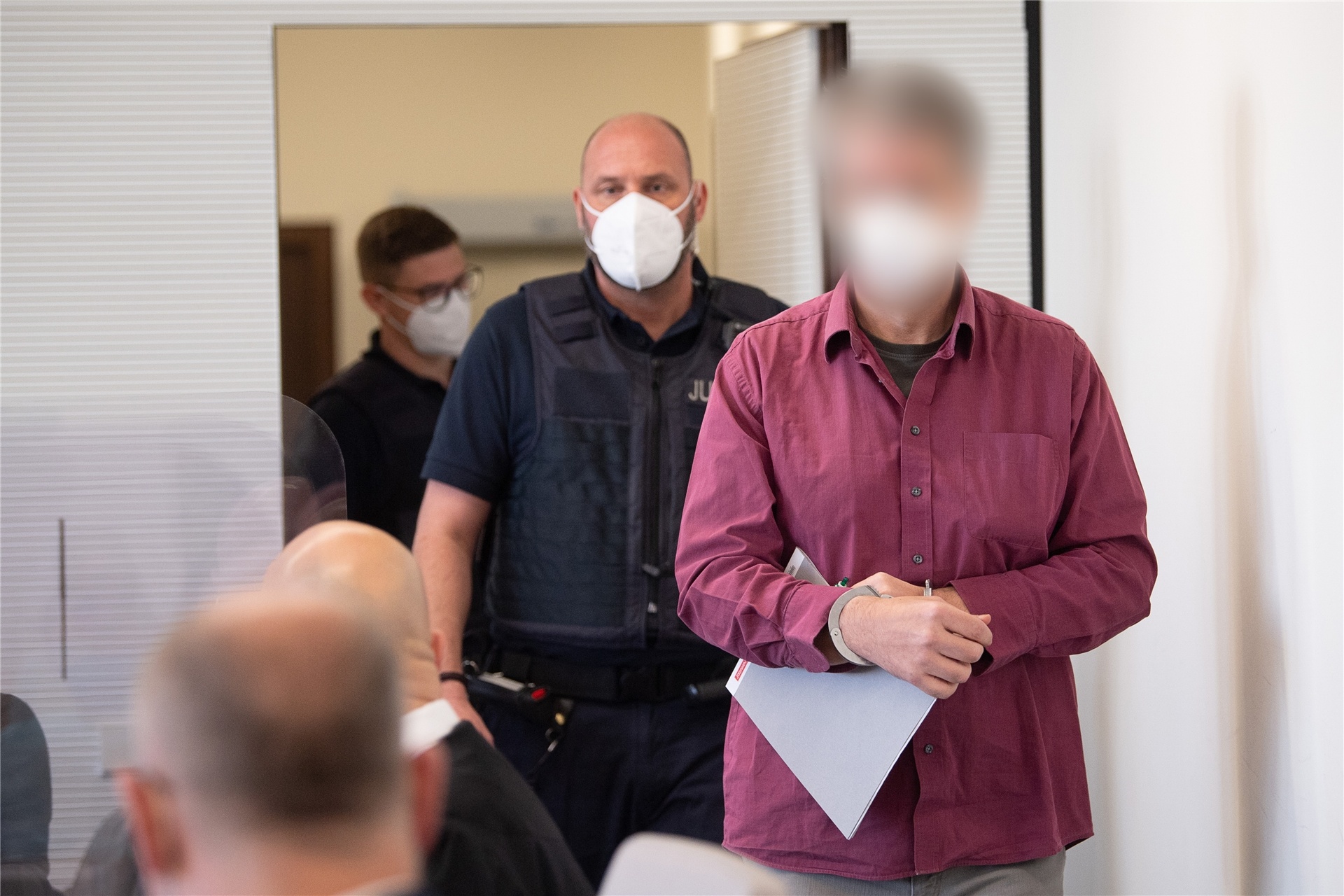 Der Angeklagte (r) wird in Handschellen in den Gerichtssaal gebracht. Der Mann hat die Tat gestanden, im vergangenen Jahr in Bad Kreuznach einen Mitarbeiter einer Tankstelle erschossen zu haben, nachdem dieser ihn auf die coronabedingte Maskenpflicht hingewiesen hatte.