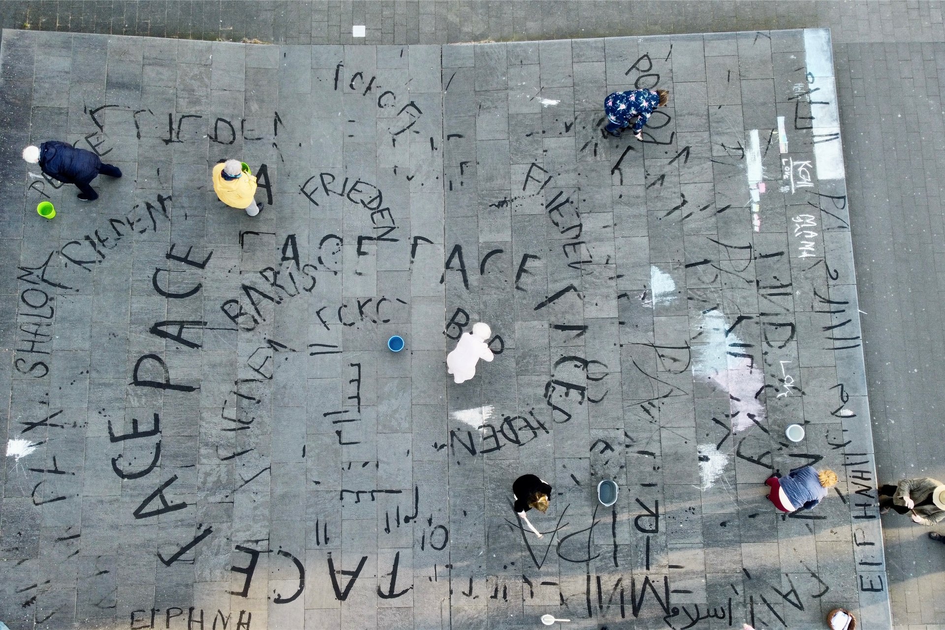 Mit Wasser schreiben Frauen der Schreibwerkstatt in vielen Sprachen das Wort „Frieden“ auf den „Bodenflügel“ vor dem Rathaus. Einige Passanten machten spontan mit, sodass auch arabische Schriftzeichen zu sehen sind.