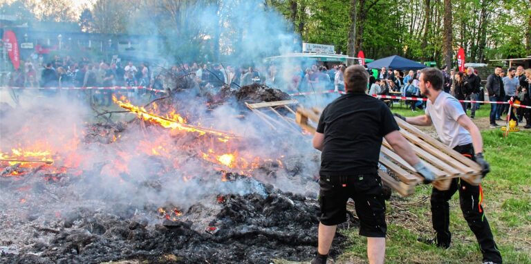 Zwei Männer werfen Holz in das brennende Osterfeuer auf dem Vereinsgelände des Jugendvereins JOE in Oer-Erkenschwick.