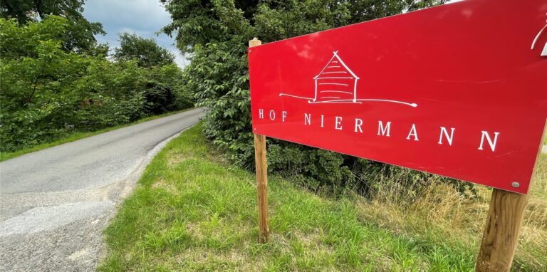 Ein rotes Schild weist auf den Waltroper Hof Niermann hin – im Hintergrund ist ländliche Umgebung zu sehen.