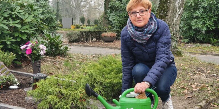 Gerda Schanzmann kniet auf dem Waldfriedhof in Oer-Erkenschwick neben einem Grab und hält eine Gießkanne.