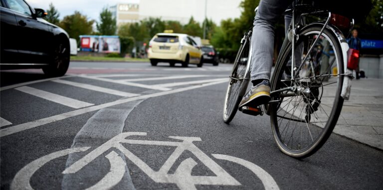 Ein Fahrradfahrer benutzt einen Radweg, im Hintergrund fahren Autos vorbei.