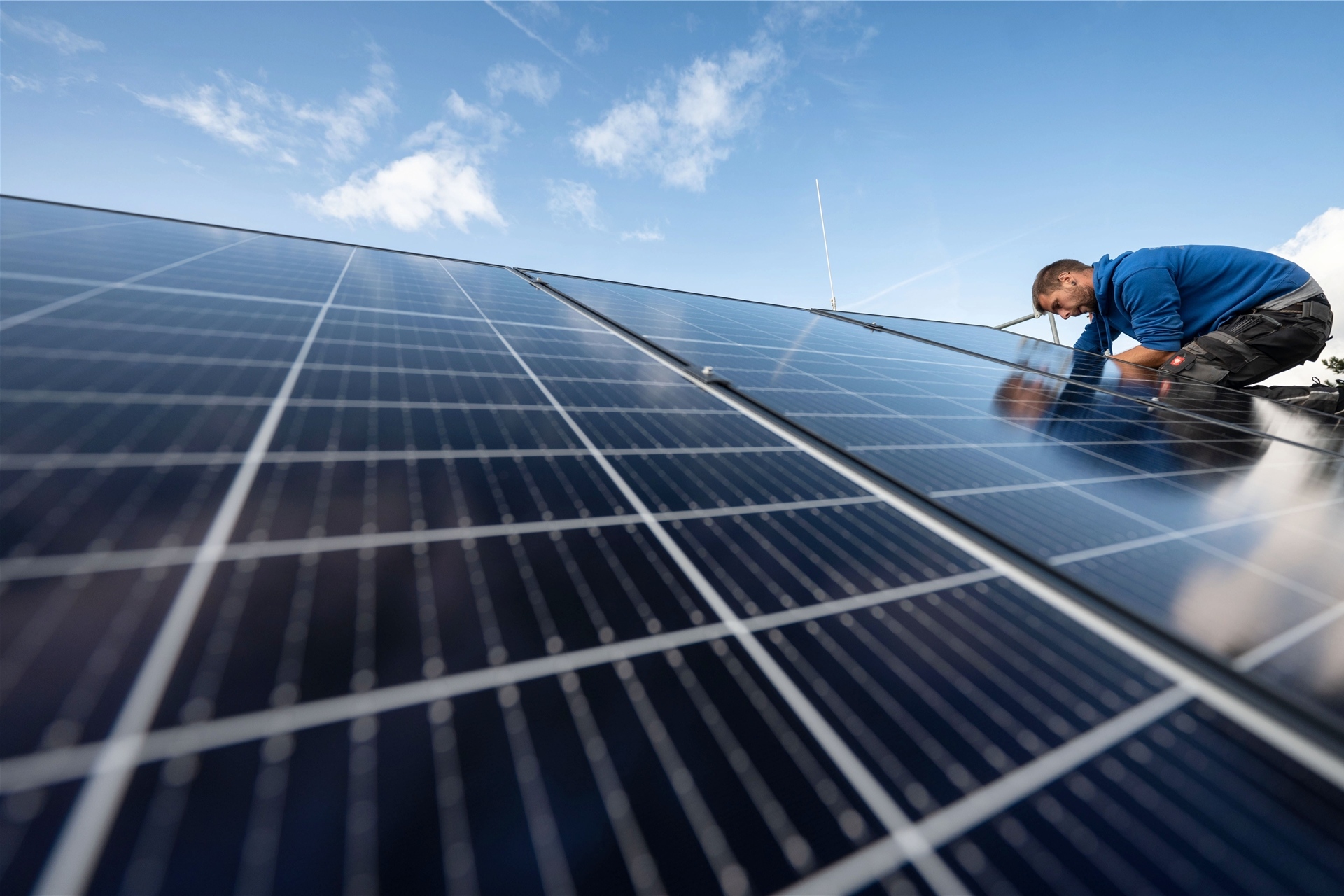 Ein Mann montiert Photovoltaikmodule auf dem Dach eines Wohnhauses.