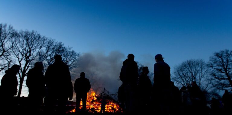 Silhouetten von Menschen, die im März 2016 in der Dämmerung vor dem Osterfeuer auf einer Wiese im Stadtteil Speckhorn in Recklinghausen stehen.