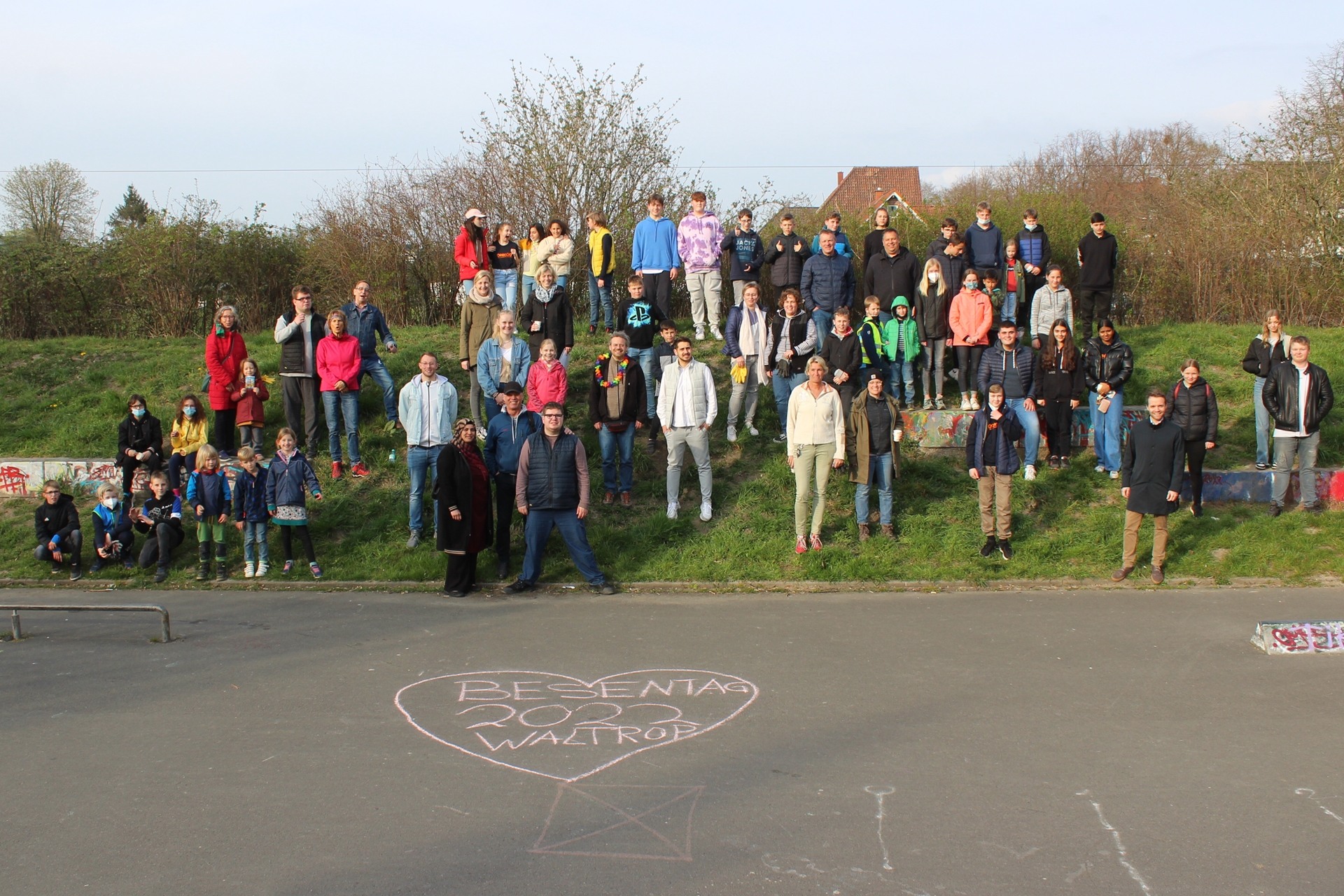 Auf einem kleinen Hügel am Cliquentreff haben sich einige Helferinnen und Helfer des Besentags des Kinder- und Jugendparlaments versammelt. Im Vordergrund ist mit Kreide „Besentag 2022 Waltrop“ in einem Herz auf den Asphalt geschrieben.