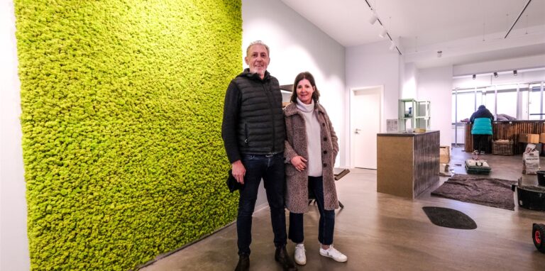 Norbert und Rita Colen stehen in ihrem noch nicht fertig eingerichteten Ladenlokal vor einer grünen Mooswand.