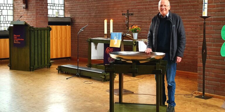 Pfarrer Bernd Schäfer steht am Taufbecken in der Friedenskirche in Oer-Erkenschwick. Im Hintergrund ist der Altar zu sehen.