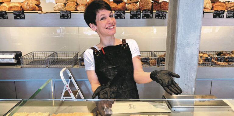 Eine junge Frau präsentiert die Bäckerei-Auslage mit verschiedenen Kuchensorten.