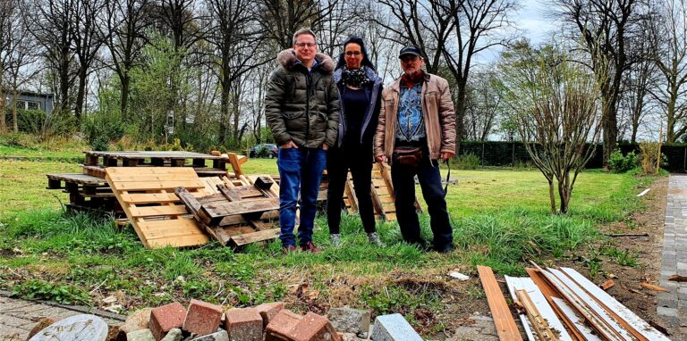 Sebastian Cuvelier, Michaela Bürger und Martin Perenz stehen auf dem Außengelände des „JOE’s“ in Oer-Erkenschwick, neben ihnen türmt sich das erste Brennmaterial für das Osterfeuer auf.