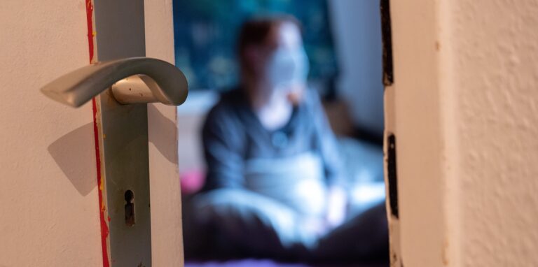 Eine Frau sitzt während der Isolation nach einem positiven Corona-PCR-Test auf ihrem Bett.