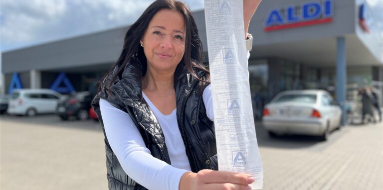 Sandra Westerholt hält einen langen Kassenbon in die Kamera. Sie steht vor dem Aldi.