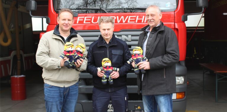 Jochen Möcklinghoff, Andreas Pust und Detlef Tzschackert von der Waltroper Feuerwehr stehen vor einem Einsatzfahrzeug und halten Traumabären – Teddybären in Feuerwehr-Montur – in der Hand.