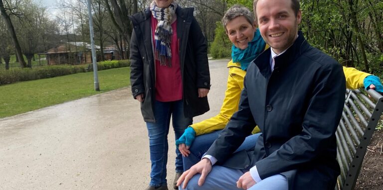 Claudia Ritzmann vom Fachbereich Umwelt und Bauen der Stadt Waltrop steht im Moselbachpark neben einer neuen Bank, auf der Sponsorin Sonja Wißemann (Firma Sonnenschein) und Bürgermeister Marcel Mittelbach sitzen.
