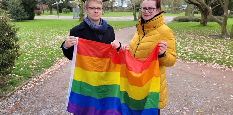 Rita Nowak und Daniel Petzoldt stehen mit einer Regenbogenflagge im Stadtpark.