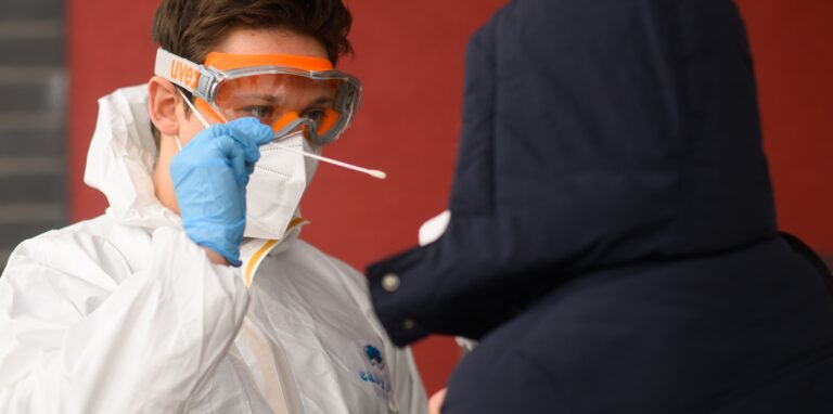 Ein Mitarbeiter nimmt einen Abstrich von einer Patientin für einen PCR-Test auf das Coronavirus vor einer Arztpraxis.