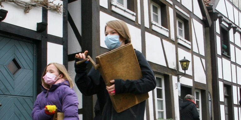 Mit Mundschutz laufen Sarah (r.) und Lina über den Ostwall im Alten Dorf Westerholt und drehen die Kurbeln ihrer hölzernen Rätteln. Das Foto entstand beim Rätteln in April 2021.