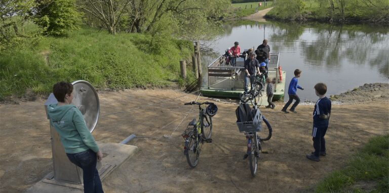 Menschen stehen am Ufer der Lippe und warten auf das Anlegen der Kurbelfähre.
