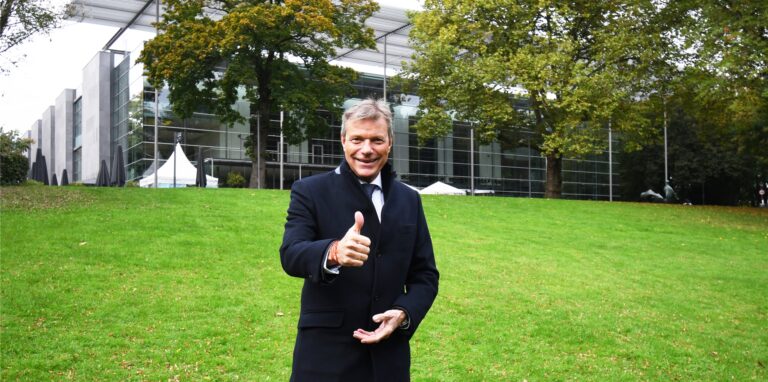 Bürgermeister Christoph Tesche steht auf der Wiese vor dem Festspielhaus und hält den Daumen nach oben.