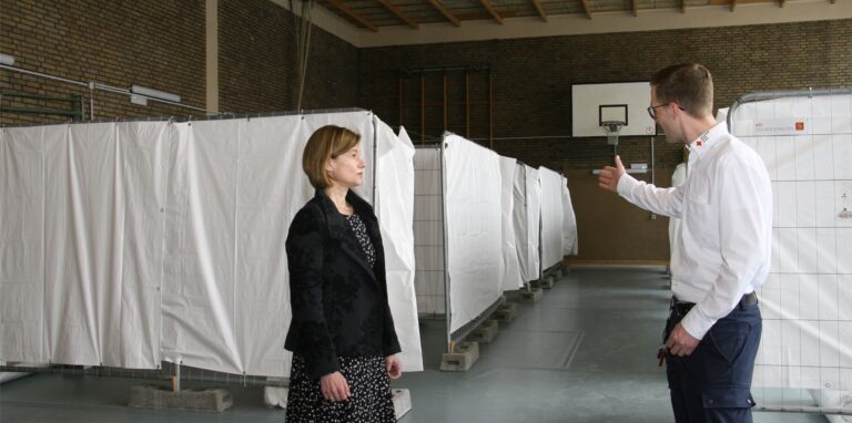 Die städtische Sozialmanagerin Uschi Dorka und Kevin Rybaczyk, Leiter Leitstelle und Einsatzdienste beim DRK Herten, besichtigen die provisorische Flüchtlingsunterkunft in der Karl-Schweisfurth-Turnhalle.