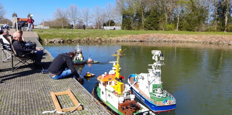 Mehrere Modell-Boote schwimmen auf dem Wasser des Oberwassers. Auf einem Steg sitzen mehrere Mitglieder des Schiffsmodellbauclubs Waltrop.