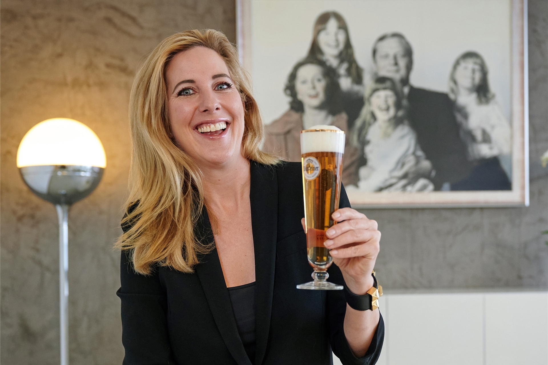 Catharina Cramer, Inhaberin des Brauerei-Unternehmens Warsteiner, sitzt mit einem Glas Bier in ihrem Büro. Im Hintergrund hängt ein Familienfoto, auf dem sie bei ihrem Vater Albert auf dem Schoß sitzt.