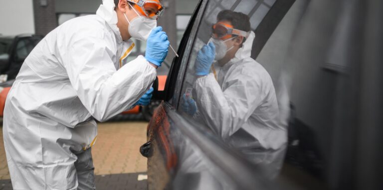 Ein Mitarbeiter entnimmt einen Abstrich von einem in einem Auto sitzenden Patienten für einen PCR-Test auf das Coronavirus vor einer Arztpraxis.