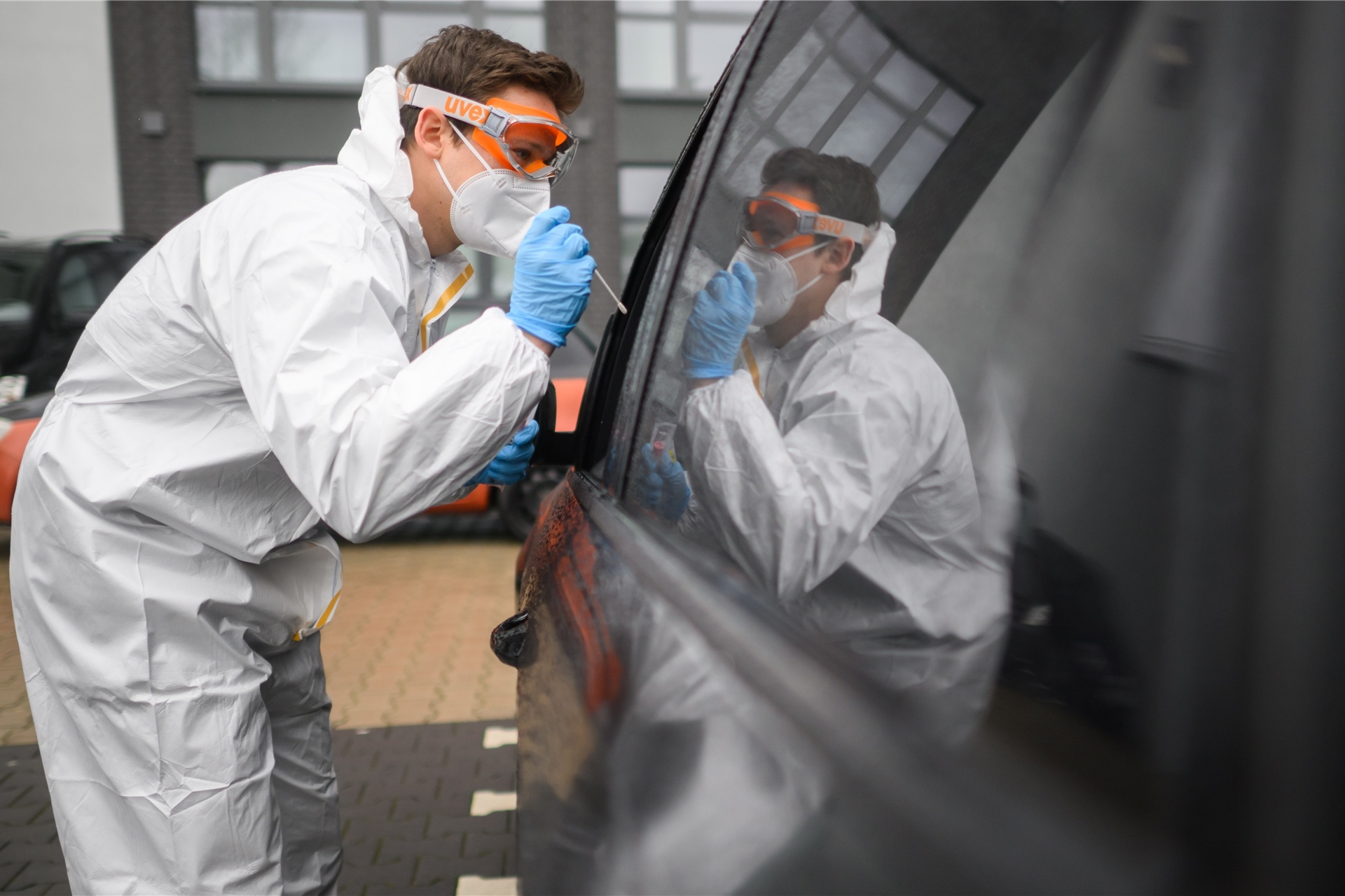 Ein Mitarbeiter entnimmt einen Abstrich von einem in einem Auto sitzenden Patienten für einen PCR-Test auf das Coronavirus vor einer Arztpraxis.