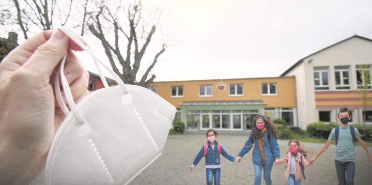 Menschen laufen mit Corona-Schutzmasken über einen Schulhof.