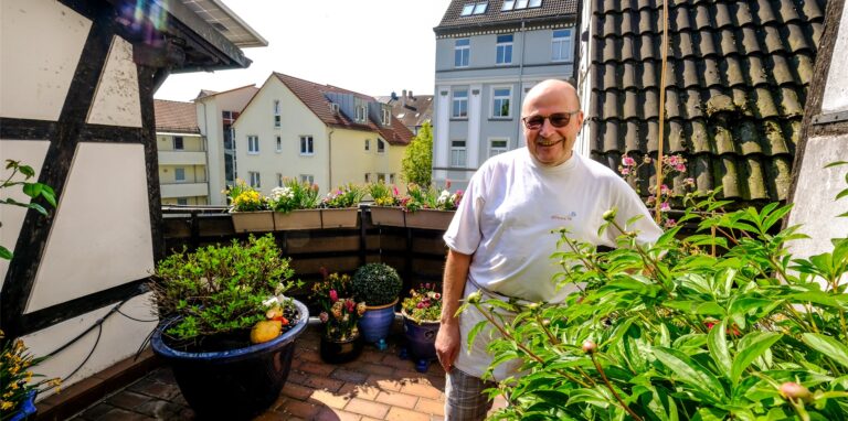 Ein Mann mit weißem T-Shirt und Brille steht auf einer Dachterrasse