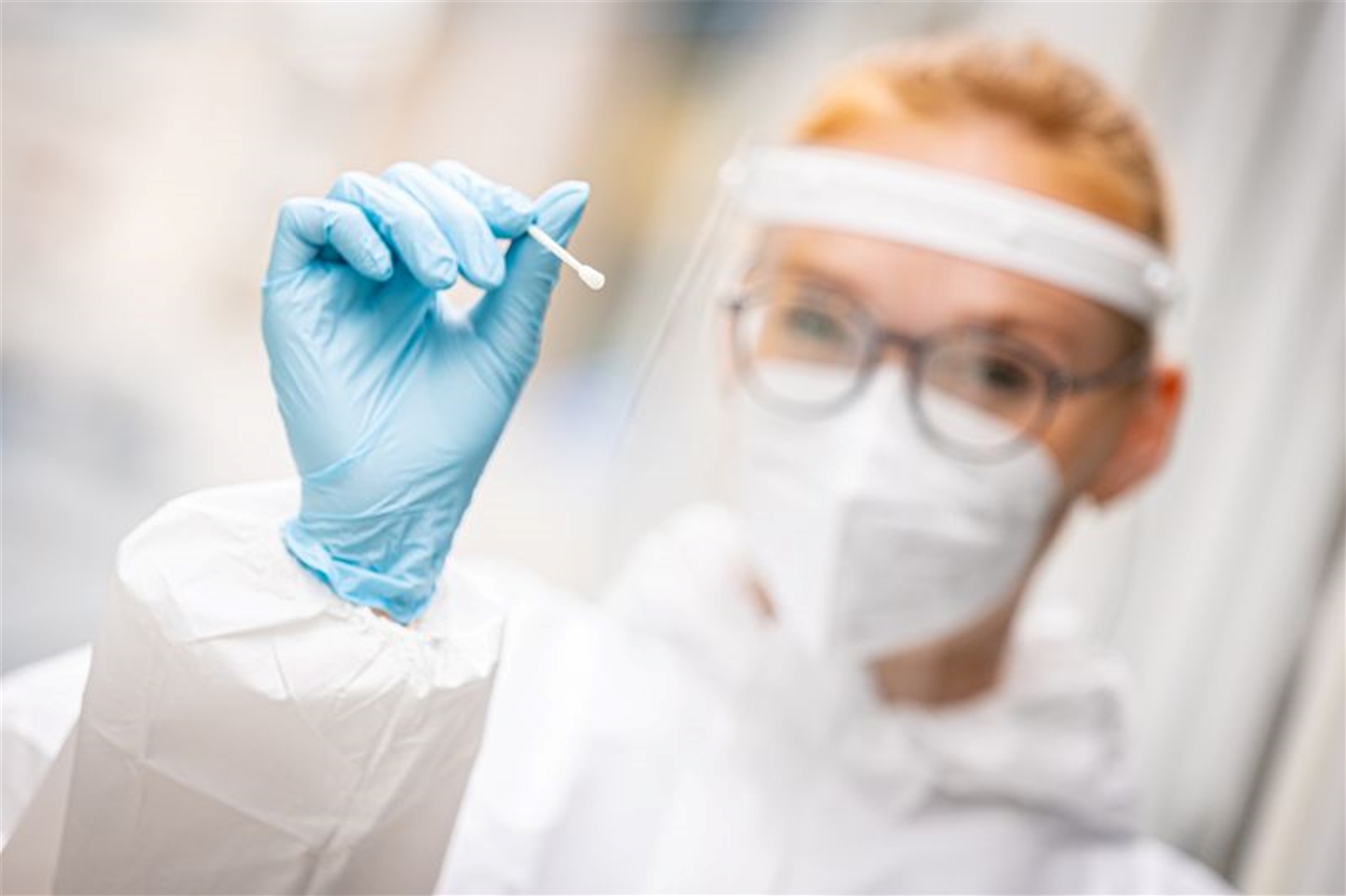 Eine Frau in Schutzkleidung und mit Maske hält einen Tupfer in der Hand.