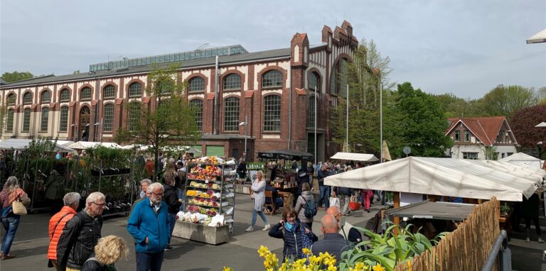 Die Gebäude von Manufactum auf dem alten Zechengelände Waltrop bilden die Kulissen für diverse Pflanzen-Marktstände der „Gartentage“. Einige Leute schauen sich um.