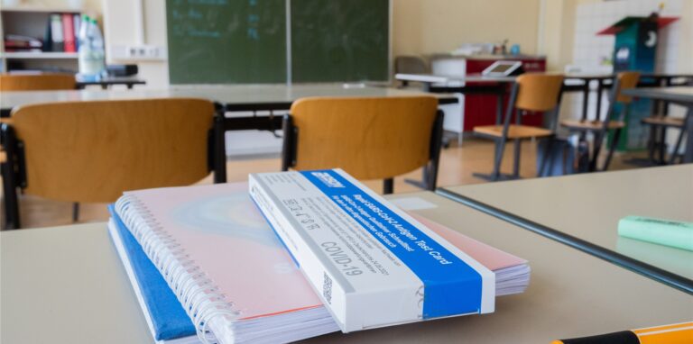 Coronatest-Packung liegt auf einem Schulheft.