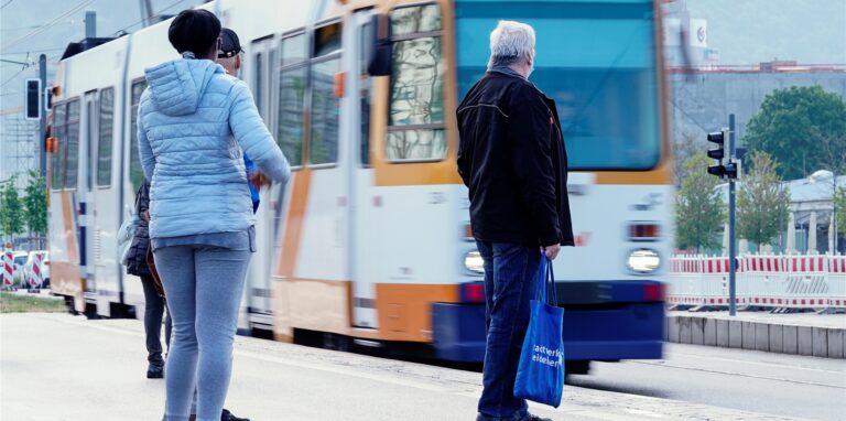 Menschen warten an einer Straßenbahnhaltestelle auf die Ankunft einer Straßenbahn. (Symbolbild)
