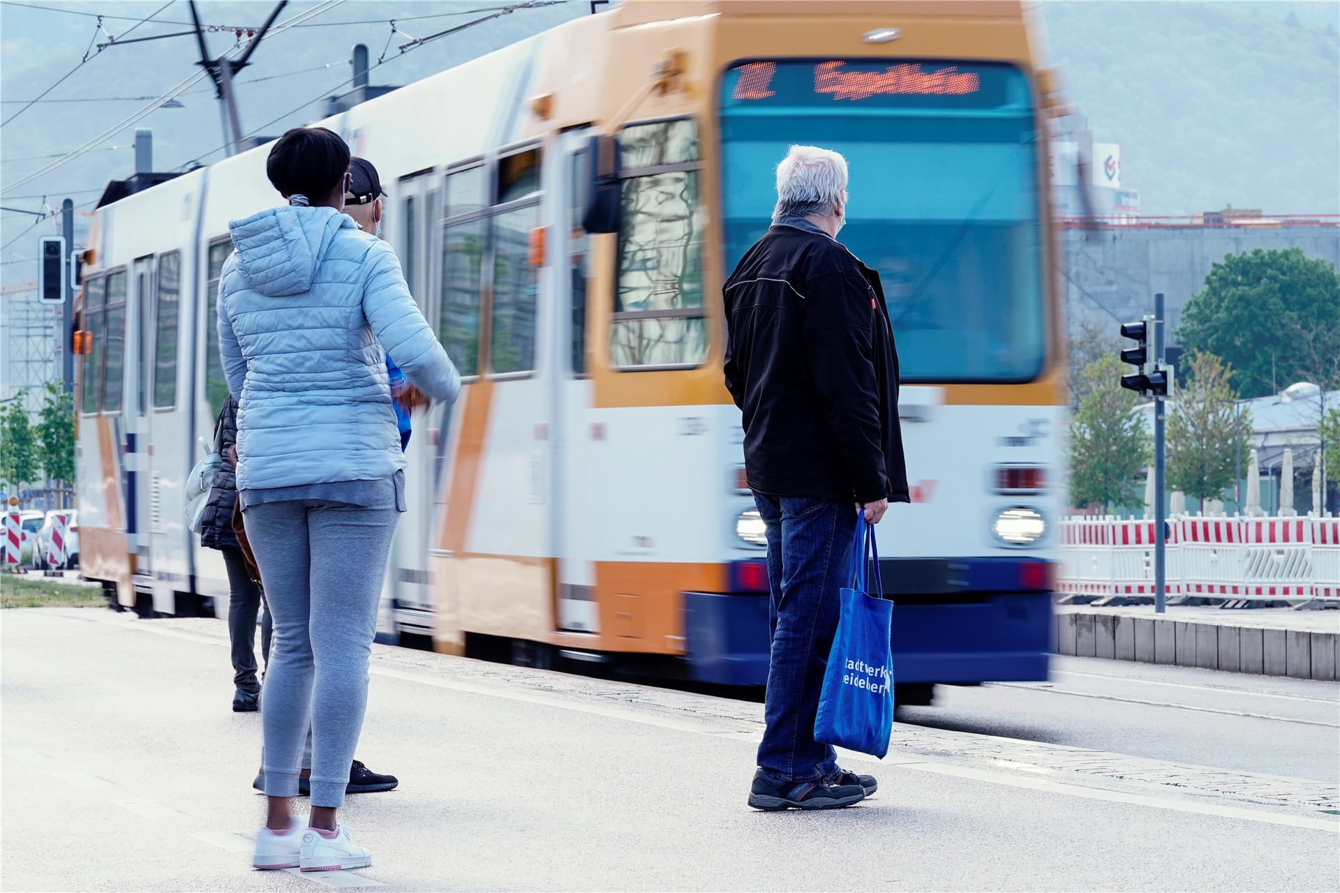 Menschen warten an einer Straßenbahnhaltestelle auf die Ankunft einer Straßenbahn. (Symbolbild)
