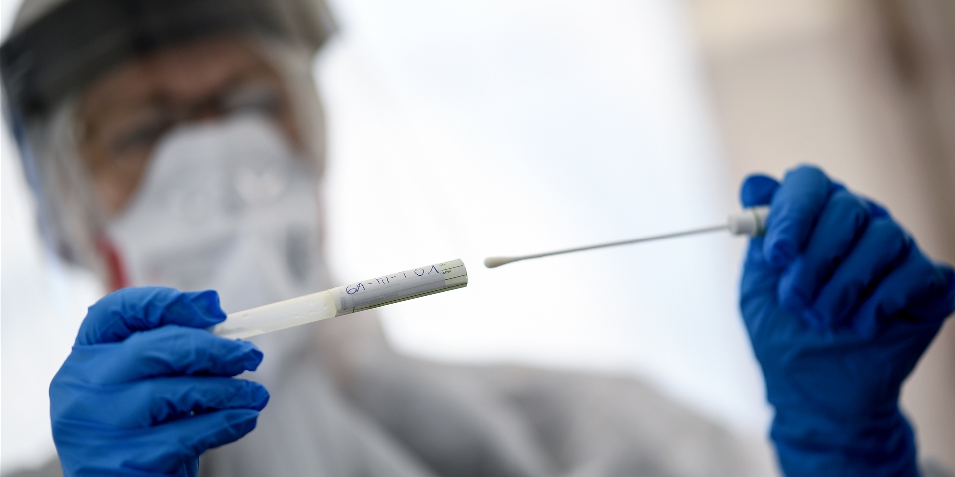 Ein Mann in Schutz-Montur führt einen Coronatest durch und hat entsprechende Röhrchen in den Händen.