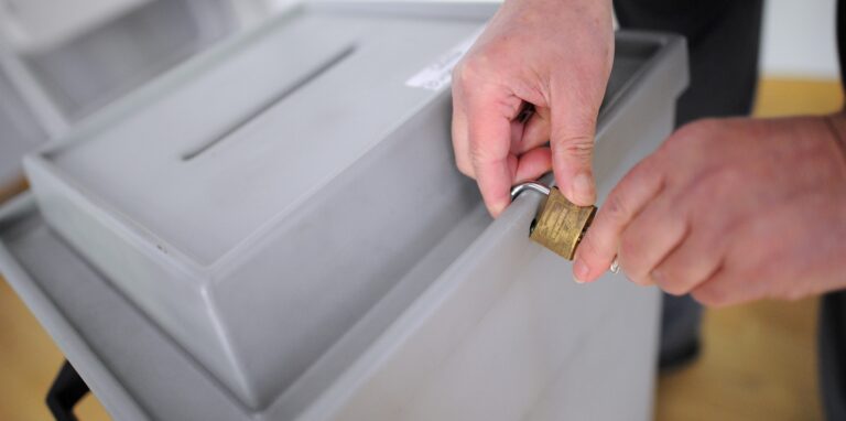 Ein Wahlhelfer verschließt eine Wahlurne mit einem Vorhängeschloss. In Herten laufen die Personalplanungen für den Tag der Entscheidung am 15. Mai auf Hochtouren.