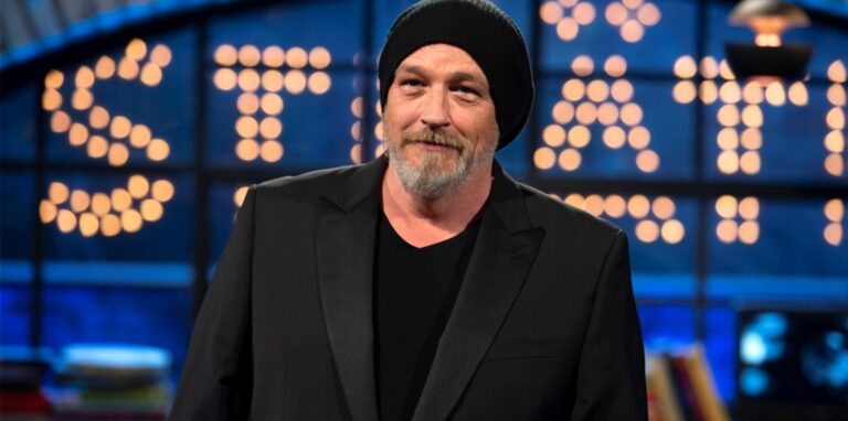 Der Waltroper Comedian Torsten Sträter ist, ganz in Schwarz gekleidet und mit seiner typischen schwarzen Mütze, vor einem Leucht-Schriftzug seiner Sendung „Sträter“ zu sehen.