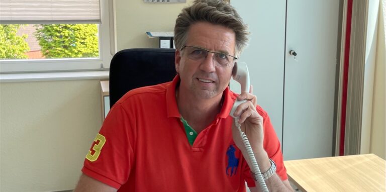 André Krywa, Geschäftsführer der Spedition Nitz in Dorsten Wulfen-Barkenberg, sitzt an einem Schreibtisch und hält ein Telefon in der Hand.
