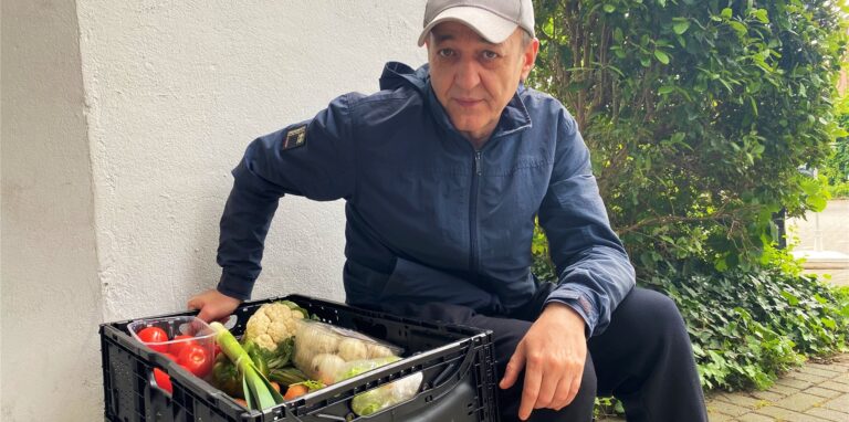 Tafel-Kunde Oleg Schefer sitzt neben einer Gemüsekiste.