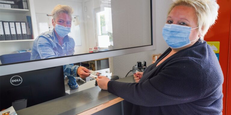 Eine Frau zeigt an einem Schalter einen Ausweis vor, den eine andere Frau kontrolliert.