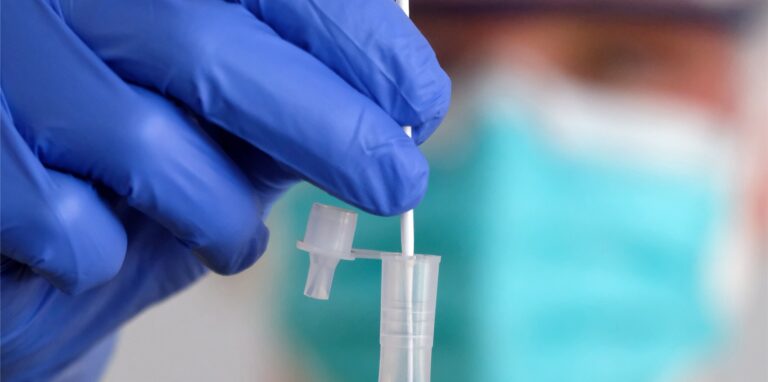 Eine Hand hält eine Coronatest-Probe. 