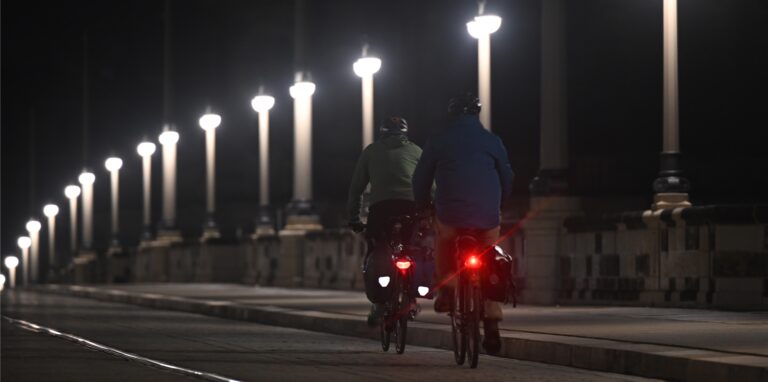 Fahrradfahrer fahren am Morgen über die sanierte Augustusbrücke an LED Lampen entlang.