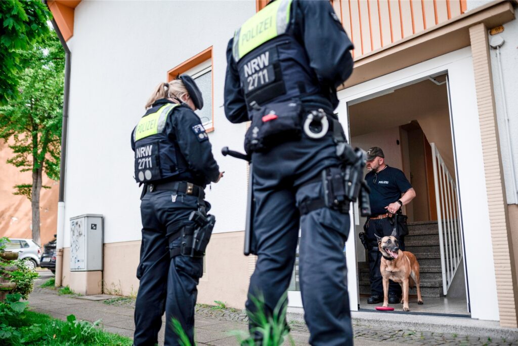 Ein Polizist mit Spürhund steht im Hauseingang des Tatverdächtigen in Essen. Ein Polizist mit Spürhund steht im Hauseingang des Tatverdächtigen in Essen.