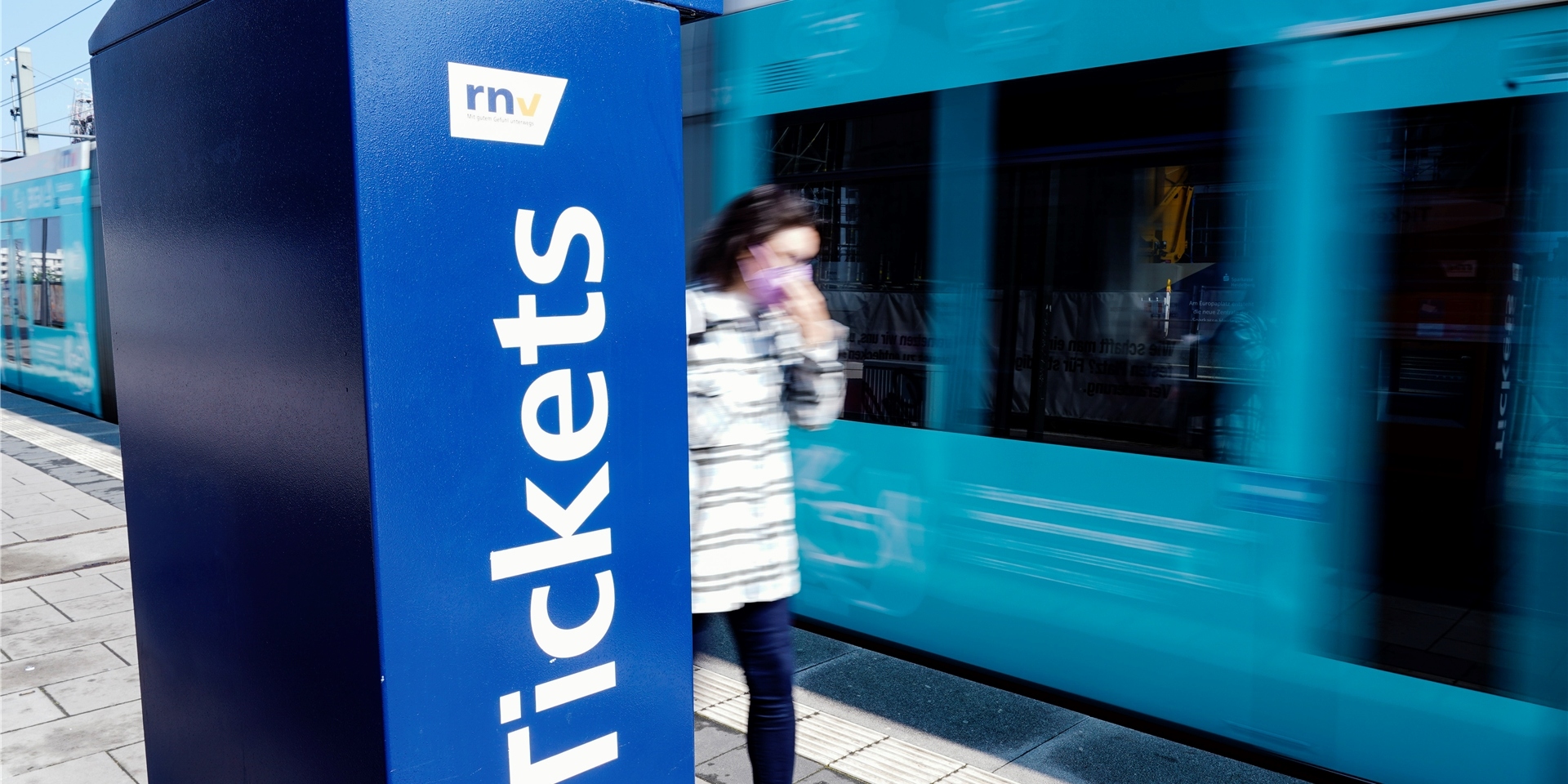Eine Straßenbahn fährt an einer Straßenbahnhaltestelle an einem Ticketautomaten vorbei.