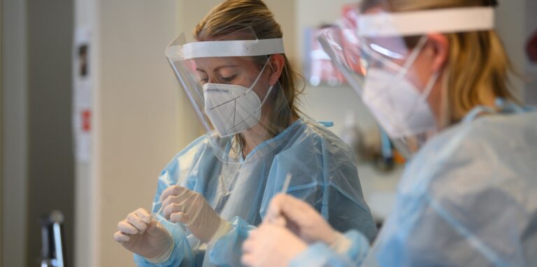 Eine Frau im Schutzkittel und mit Maske wertet einen Antigen-Schnelltest auf das Coronavirus aus.