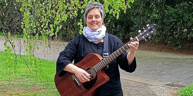 Singleiterin Claudia Kock spielt auf einer Gitarre und geht dabei einen Weg entlang.