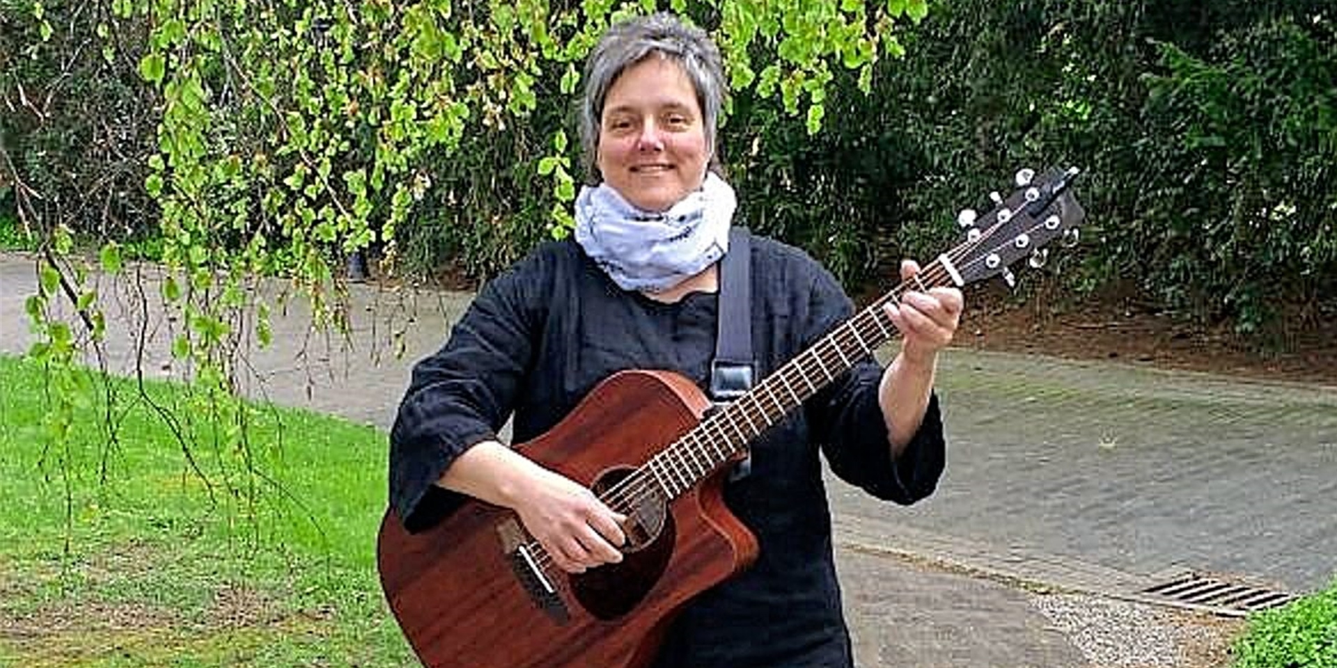 Singleiterin Claudia Kock spielt auf einer Gitarre und geht dabei einen Weg entlang.