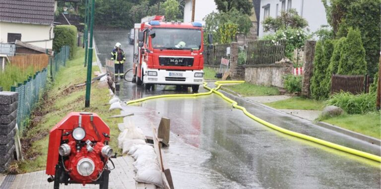 Feuerwehrleute haben auf einer Dorfstraße nach heftigen Regenfällen Pumpen aufgestellt.)