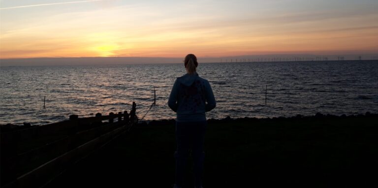 Die 19-jährige Sonya aus Haltern steht am Meer vor einem Sonnenuntergang.