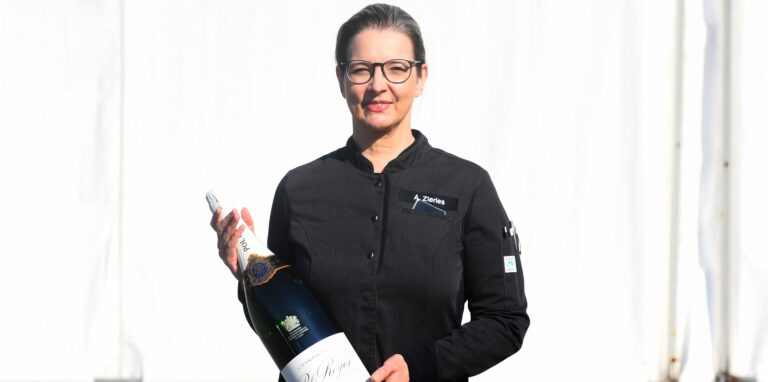 Anja Zierles hält eine große Sektflasche in den Händen.